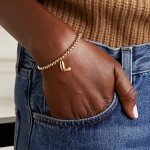 Detailed view of 18k gold beaded elastic bracelet with a rounded letter L charm on wrist