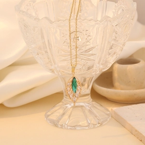 Golden leaf pendant necklace with green and white crystals on a crystal glass stand