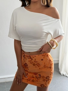 Detailed view of white one-shoulder crop top and sequined orange mini skirt on a model