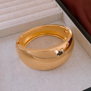 Detailed close-up of wide polished gold bangle with side hinge closure on jewelry tray