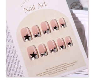 Detail of nude pink press-on nails with black stars and silver French tips on a card