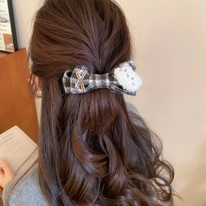 Close-up of a plush bear and plaid bow hair clip worn on long wavy hair in daily life