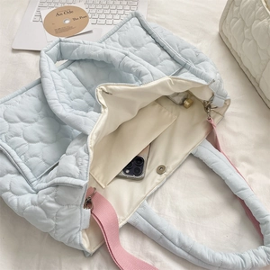 Detail of light blue quilted tote bag interior with beige pocket on white bedding