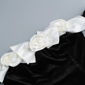 Detailed view of white satin 3D flower embellishments on a black velvet dress neckline
