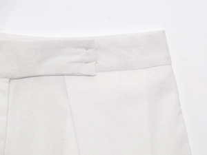Macro detail of high-quality white pleated trousers showing fine fabric texture and stitching
