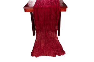 Close-up of deep red wrinkled cheesecloth table runner draped on a dark wood surface