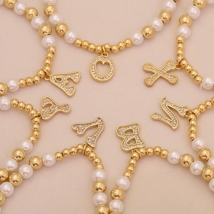 Detailed view of beaded bracelets with faux pearls, gold beads, and zircon letter charms