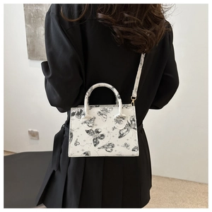 Detail of white butterfly print crossbody bag against a dark outfit for contrast