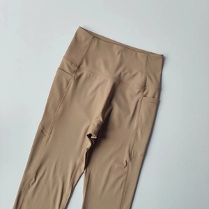 Detail of high-waist yoga leggings in camel brown with side pockets for sports