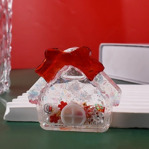 Detalle de un colgante de resina con forma de casa navideña y charms de Papá Noel y lazo