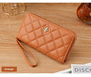 Detail of orange quilted long wallet with elegant gold flower buckle and wrist strap