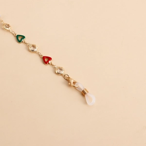 Macro detail of gold chain with red green enamel hearts and crystal accents
