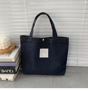 Detailed macro view of dark blue denim tote bag with cute white bear patch and silver buckle