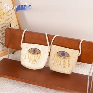 Detailed view of woven straw bags for kids with evil eye sequins and beaded tassels