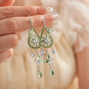 Close-up of green butterfly drop earrings with zircon flowers and tassels on metal