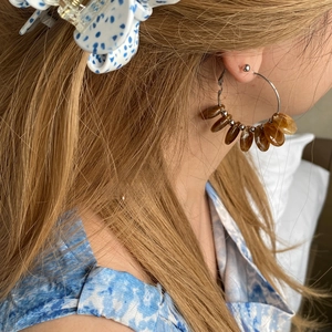 Detail of silver hoop earring with amber resin drops and metal beads on model