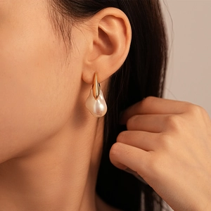 Boucle d'oreille perle baroque avec base dorée géométrique portée par un mannequin