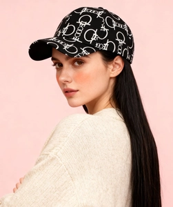 Detailed view of black baseball cap with white pattern on model in beige sweater