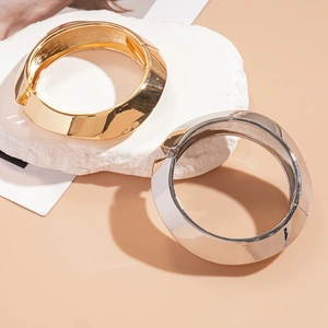 Bold geometric open bangle with wide twisted metal design in polished gold and silver finishes