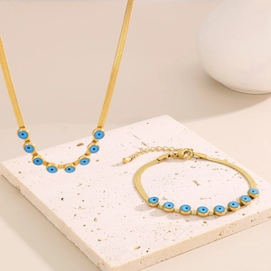 Gold snake chain jewelry set with blue evil eye charms on beige stone display