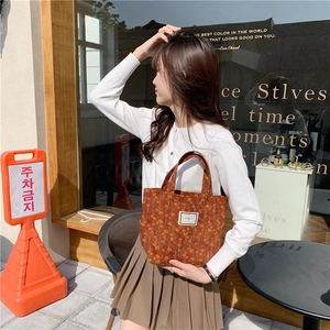 Detailed shot of brown floral corduroy tote bag held by model in casual outdoor setting