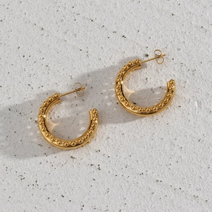 Macro detail of gold-plated C-shaped earrings with bead edges on stone background
