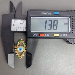 Macro shot of gold devil eye charm with zircon inlay measuring 13.8 mm on caliper