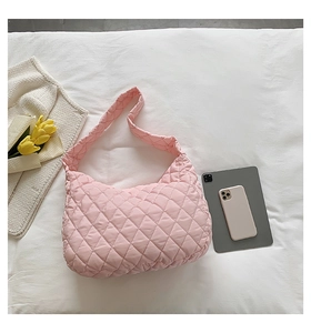 Pink quilted crossbody bag displayed on a white bed with a tablet and lifestyle items