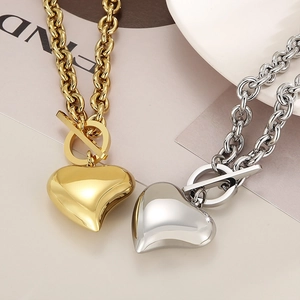 Primer plano de collares de corazón en oro y plata con cierres OT sobre un fondo elegante.