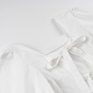 Détail du haut blanc à manches bouffantes montrant le dos nu avec un grand nœud élégant