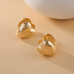 Close-up of polished 18k gold heart hoop earrings on a minimalist warm background