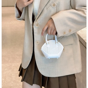 White mini shell bag with hollow weave design and gold chain strap shown on a model