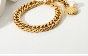 Macro detail of gold-plated Cuban chain bracelet with shell charm and freshwater pearl