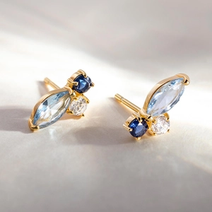 Macro shot of gold butterfly wing earrings with marquise blue stones and zircon stones
