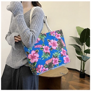 Blue canvas tote bag with pink floral print and braided rope handle shown on a model