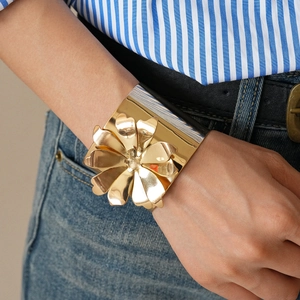 Close-up of a wide gold metal cuff bracelet featuring a large 3D mirror-finish flower