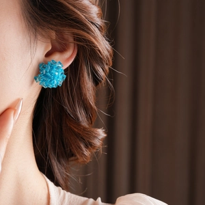 Close-up of blue glass bead flower stud earrings worn by a model in soft lighting