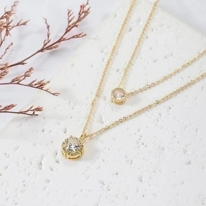 Double-layer gold necklace featuring round white zircon pendants on textured stone background