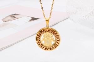Detailed close-up of golden Hamsa Hand pendant with crystal inlay on a textured frame