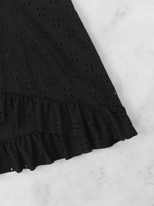 Detail of black eyelet embroidery fabric with ruffled hem on white marble background