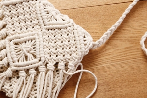 Detail einer handgefertigten Makramee-Tasche in Cremeweiß mit Knotenmustern und Fransen