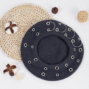 Detail shot of a dark grey wool beret with metal rings and eyelets on a clean background