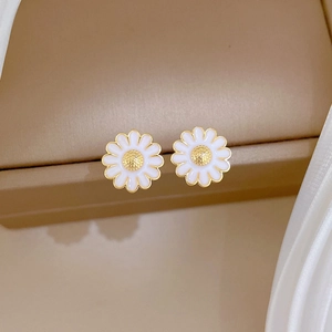 Detailed close-up of daisy stud earrings with white petals on a luxury silk and leather background
