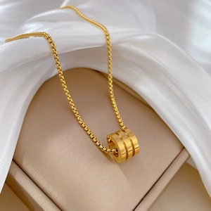 Detailed macro of gold-plated cylinder pendant on box chain over white silk fabric