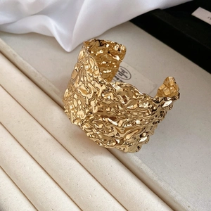 Macro detail of wide gold metal cuff bracelet featuring irregular pleated texture