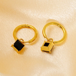 Elegant gold hoop earrings with black square zircon pendant on champagne silk fabric background