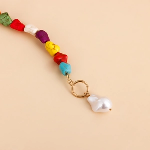 Close-up of handmade necklace with colorful natural stones and a white baroque pearl pendant