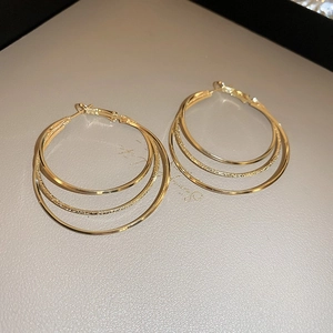 Detail of triple-hoop gold earrings with mixed mirror and frosted texture finishes
