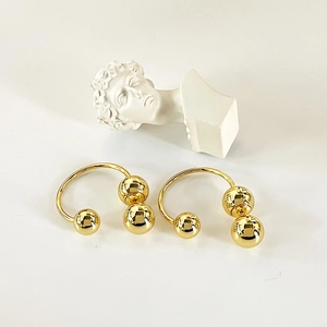 Minimalist gold arched drop earrings with polished metallic spheres on white background