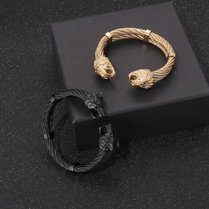 Detail of punk style lion head cable bracelets in gold and black finishes on a matte box